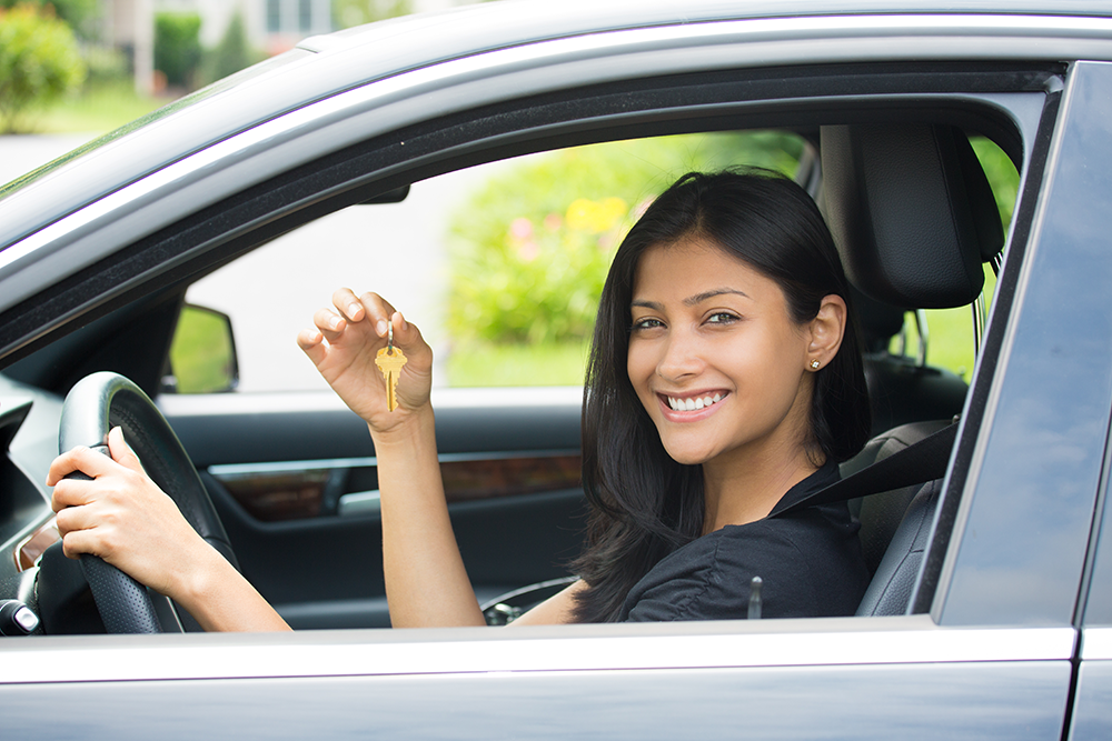 la photo montre une femme avec des clés dans la main en train de sourire. Elle se trouve au volant d'une voiture. On imagine qu'elle vient de faire l'acquisition de cette voiture. 